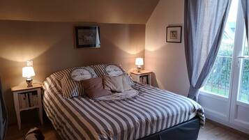 A bedroom with a bed, two bedside tables with lamps, a window with curtains, and a framed picture on the wall.