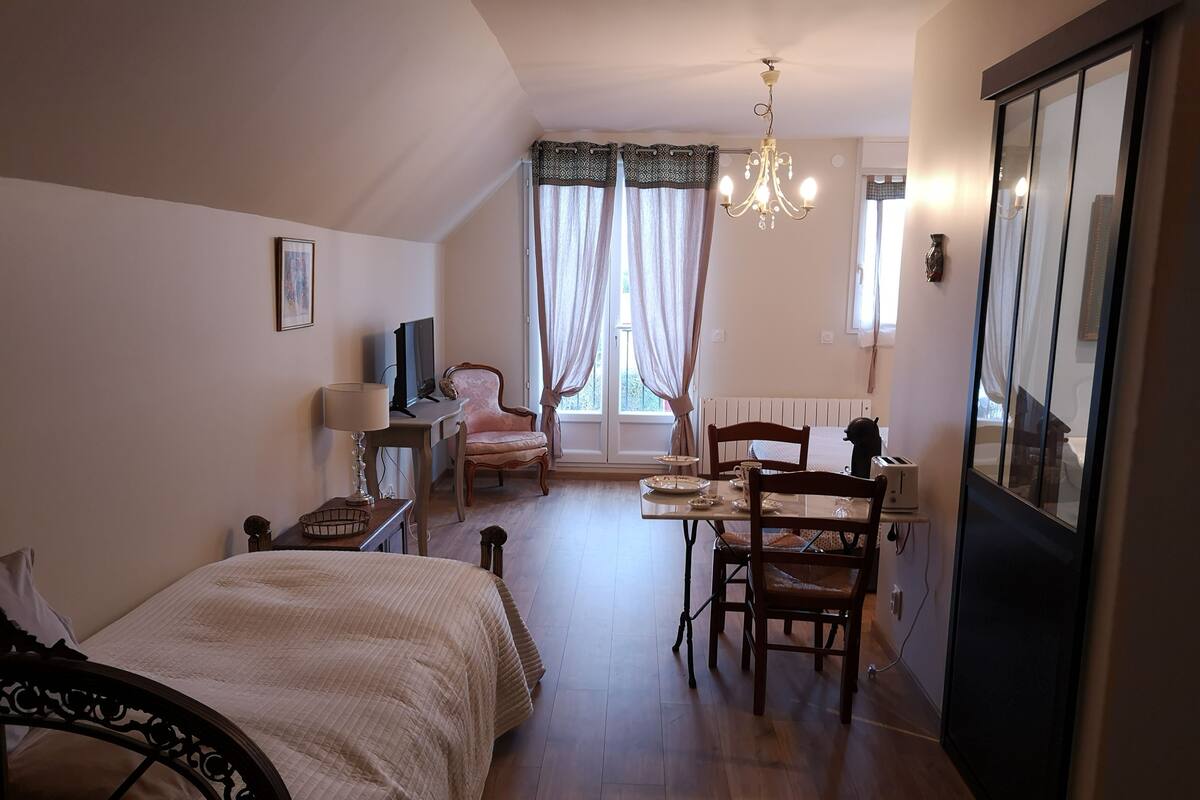 Een slaapkamer met een bed, nachtkastje, lamp, stoel, bureau en een raam met gordijnen.