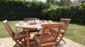 A wooden dining table set outdoors with chairs, a cloth table runner, and a fruit bowl.