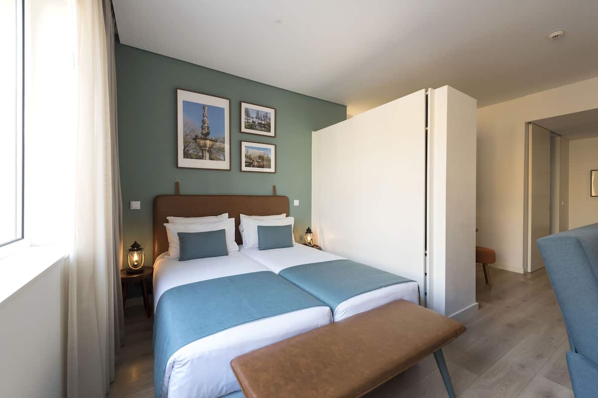 A double bed with two pillows, a bedside table with a lamp, and a bench.