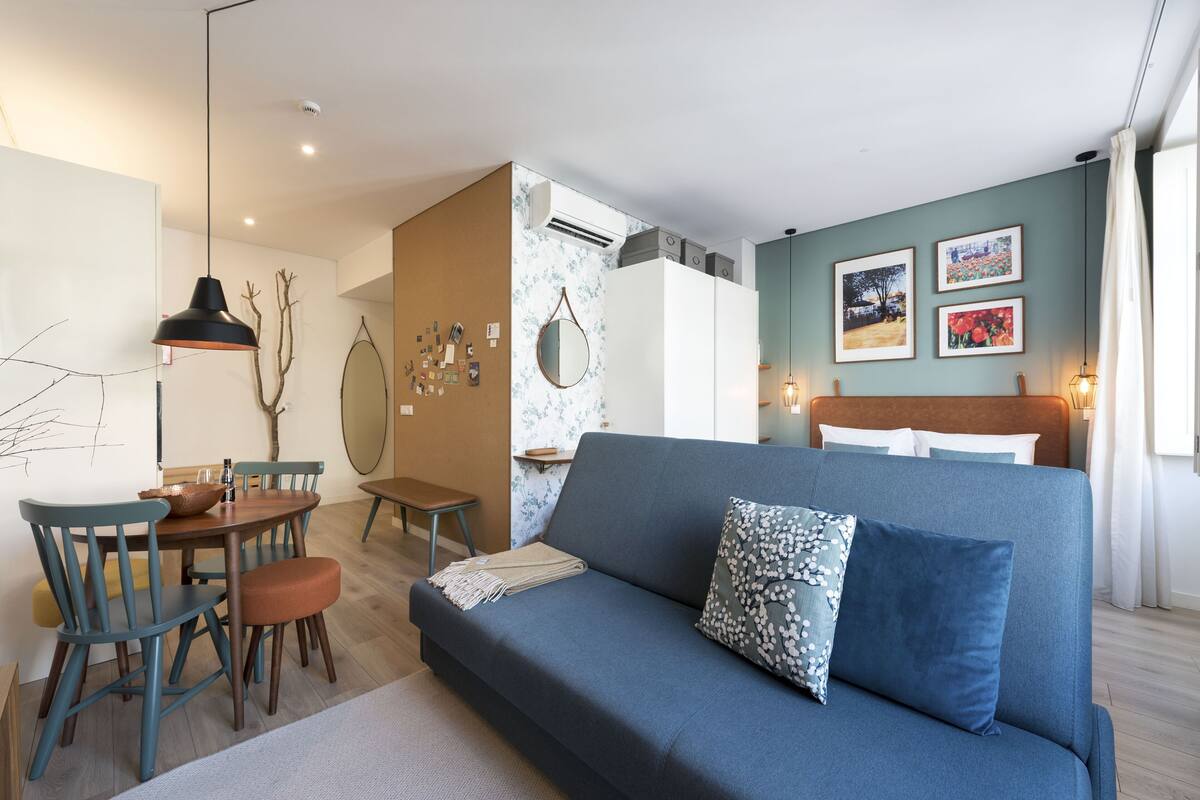 A modern living room with a sofa, dining table, chairs, and artwork on the walls.