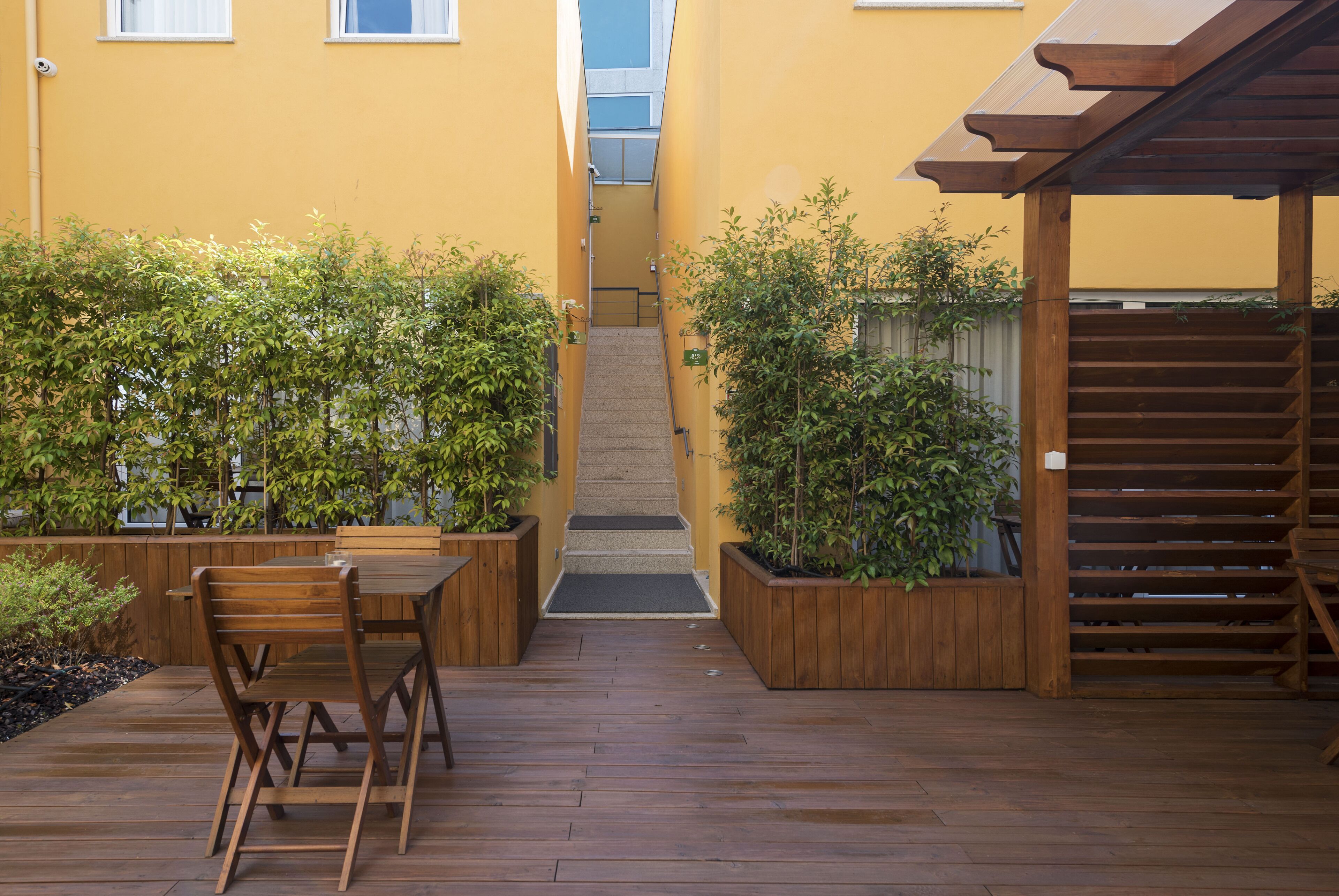 A wooden deck with a table and chairs, surrounded by potted plants and a wooden staircase.