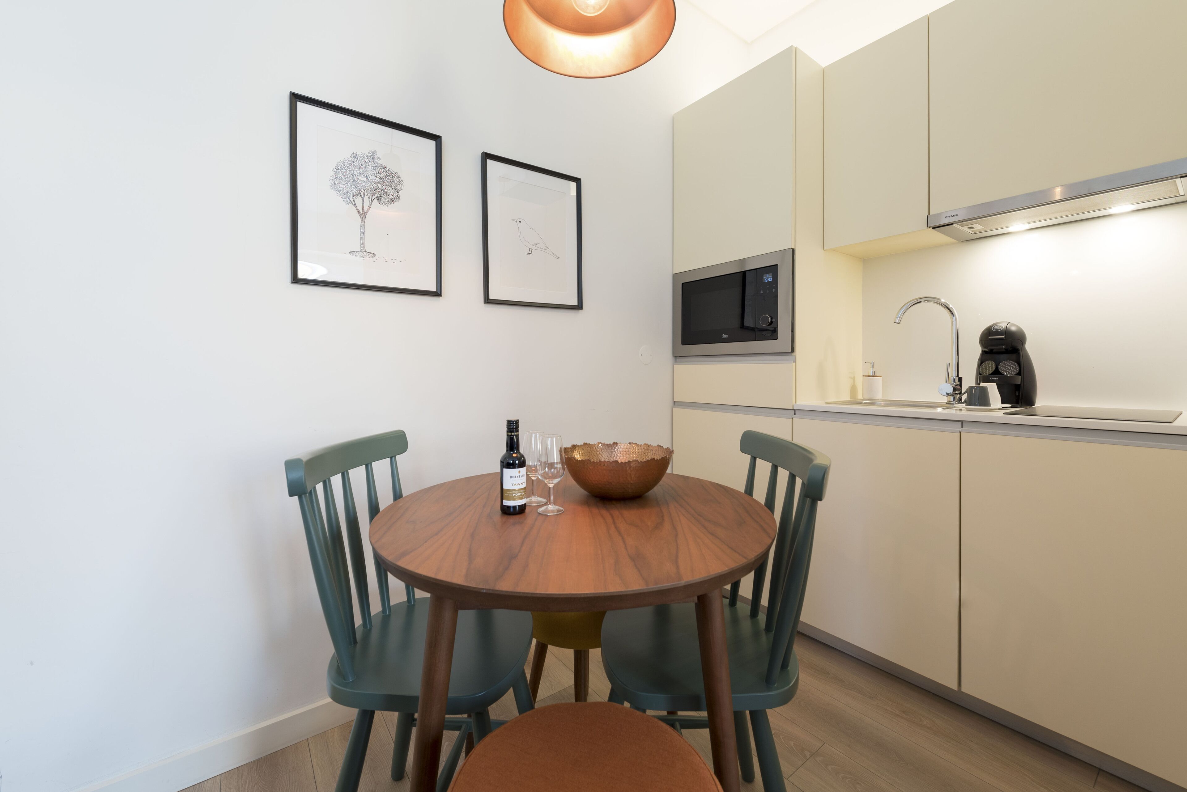 Una cocina moderna con una mesa redonda para comer, dos cuadros enmarcados y un microondas.