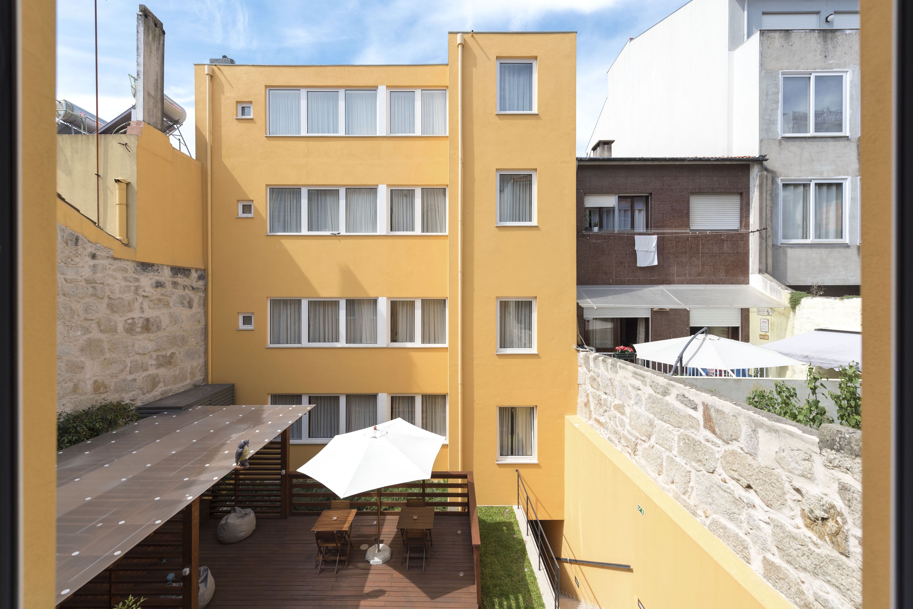 A multi-story yellow building with balconies, outdoor seating, and a stone wall.