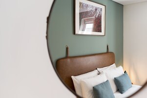 A bedroom with a brown headboard, white and blue pillows, and a framed picture on the wall.