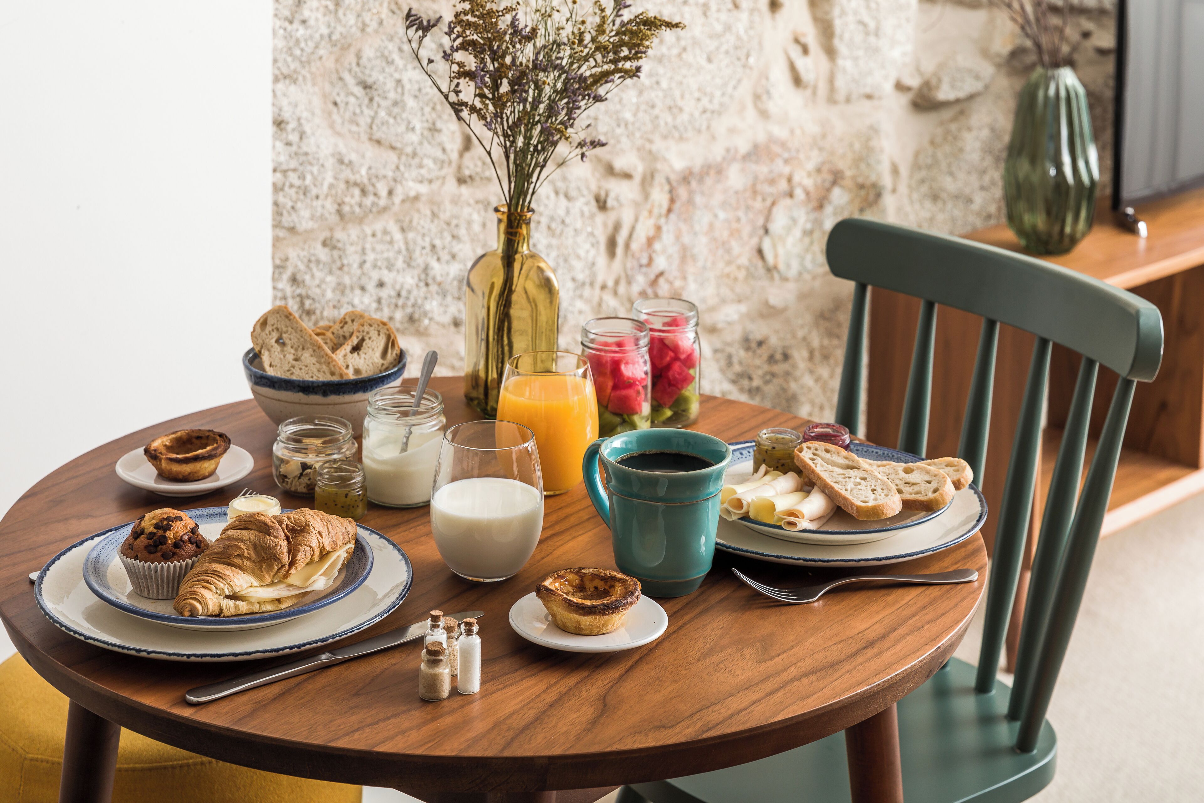 A breakfast table with croissants, muffins, a glass of milk, and a cup of coffee.