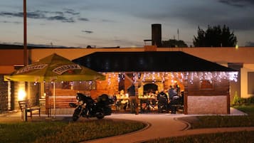 Un restaurante al aire libre con terraza techada, mesas exteriores y una motocicleta estacionada cerca.
