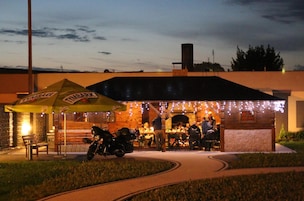 Um restaurante ao ar livre com um terraço coberto, mesas externas e uma motocicleta estacionada perto.
