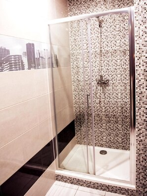 Ducha con paredes de mosaico de cerámica y cabina de vidrio.