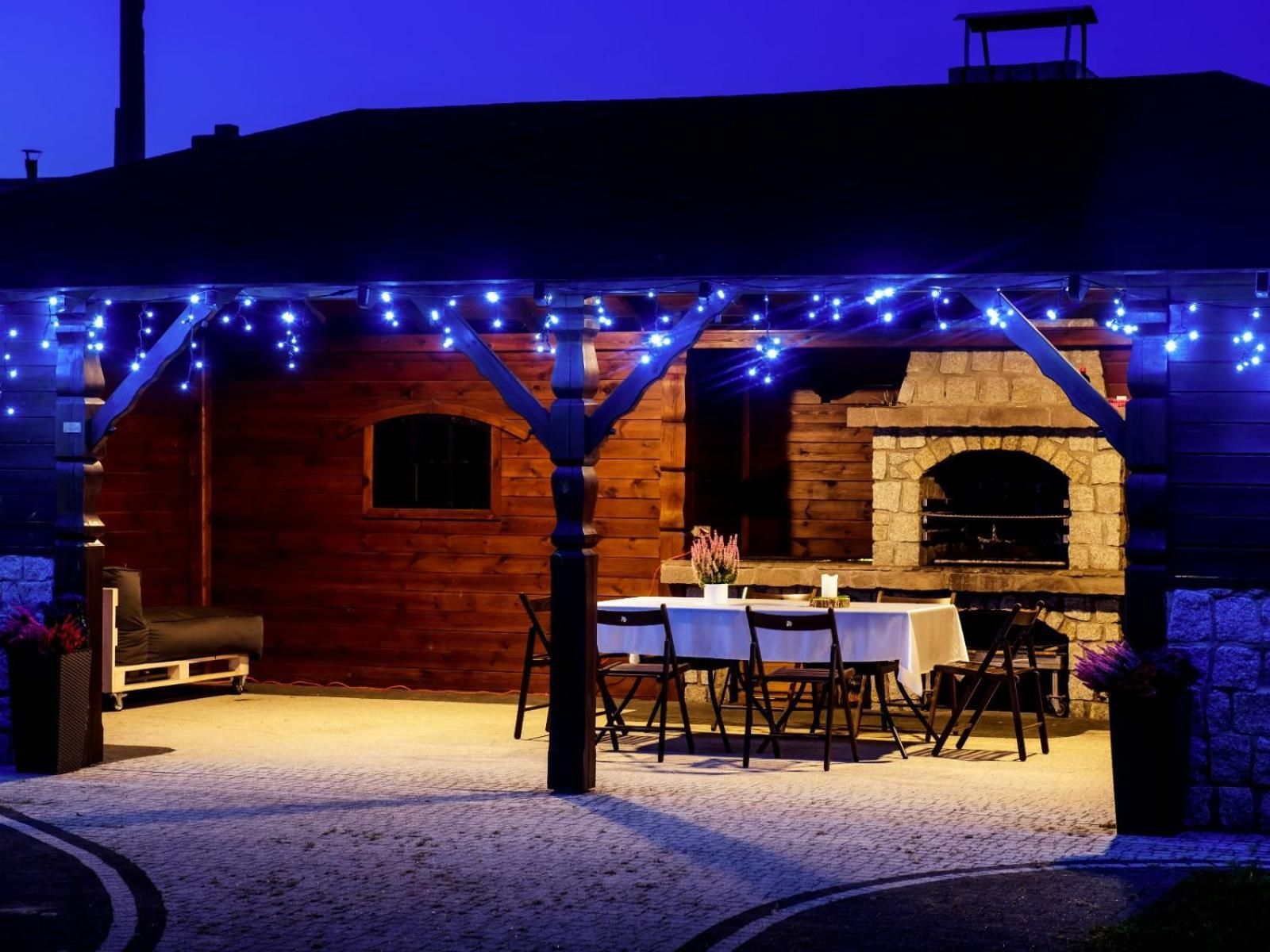 An outdoor patio with a stone fireplace, wooden walls, and string lights.