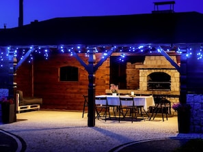 Un patio al aire libre con chimenea de piedra, paredes de madera y luces colgantes.