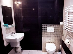 Un baño moderno con un lavamanos blanco, un inodoro y una repisa de vidrio con artículos de aseo.