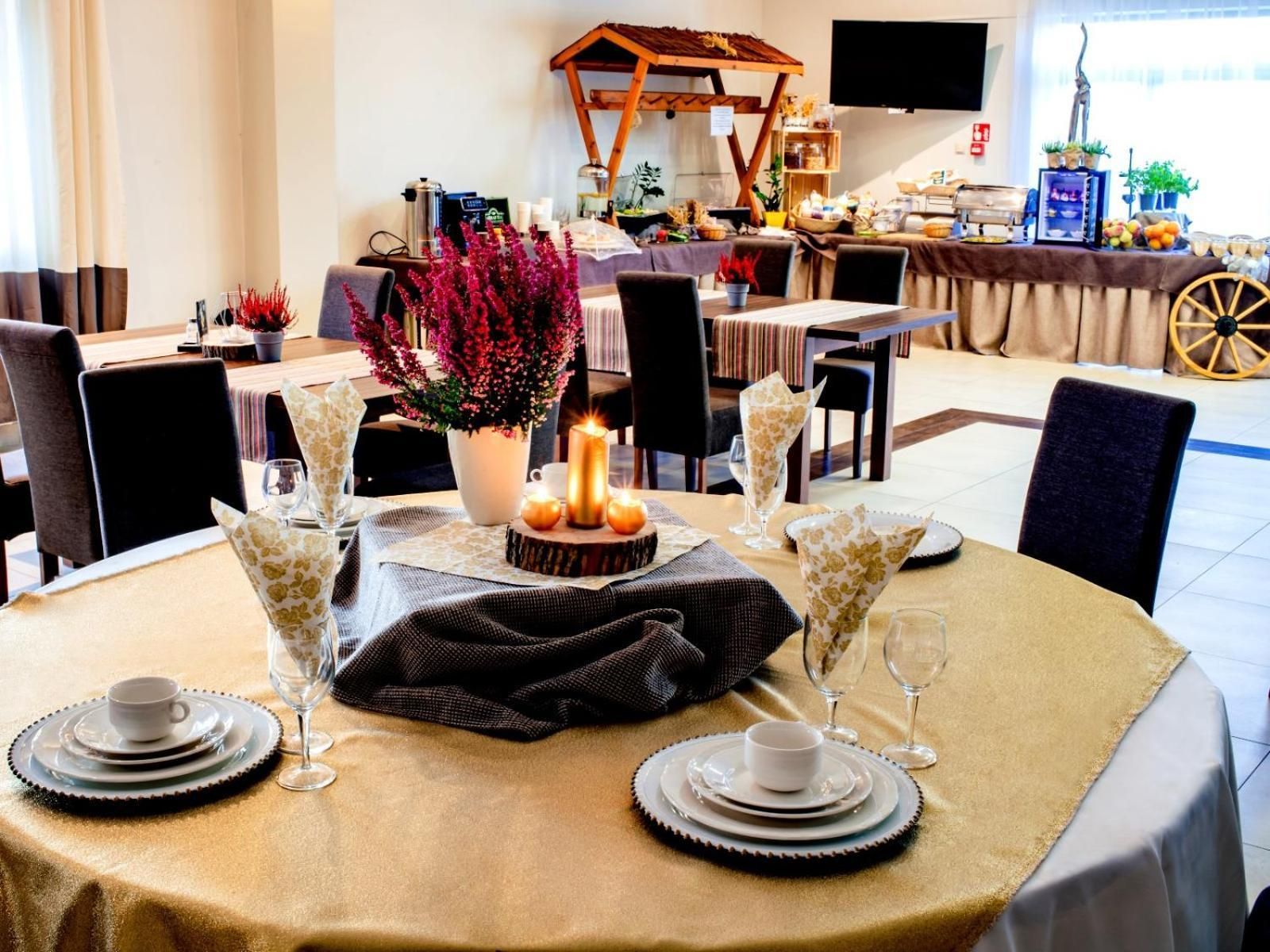 A dining area with round tables set for a meal, featuring a central floral arrangement and candles.