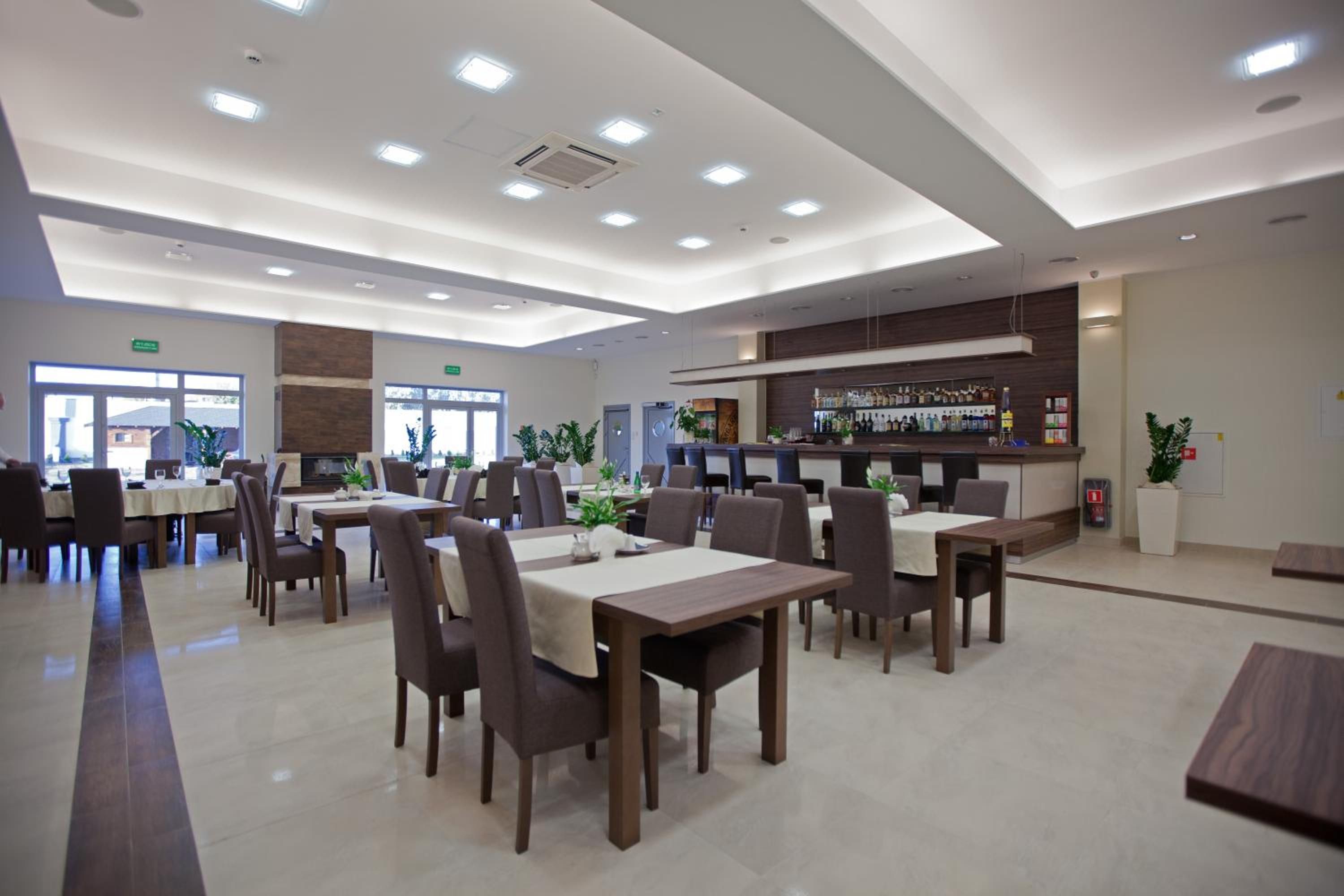 A modern dining area with multiple tables and chairs, a bar area with a variety of bottles, and a clean, well-lit interior.
