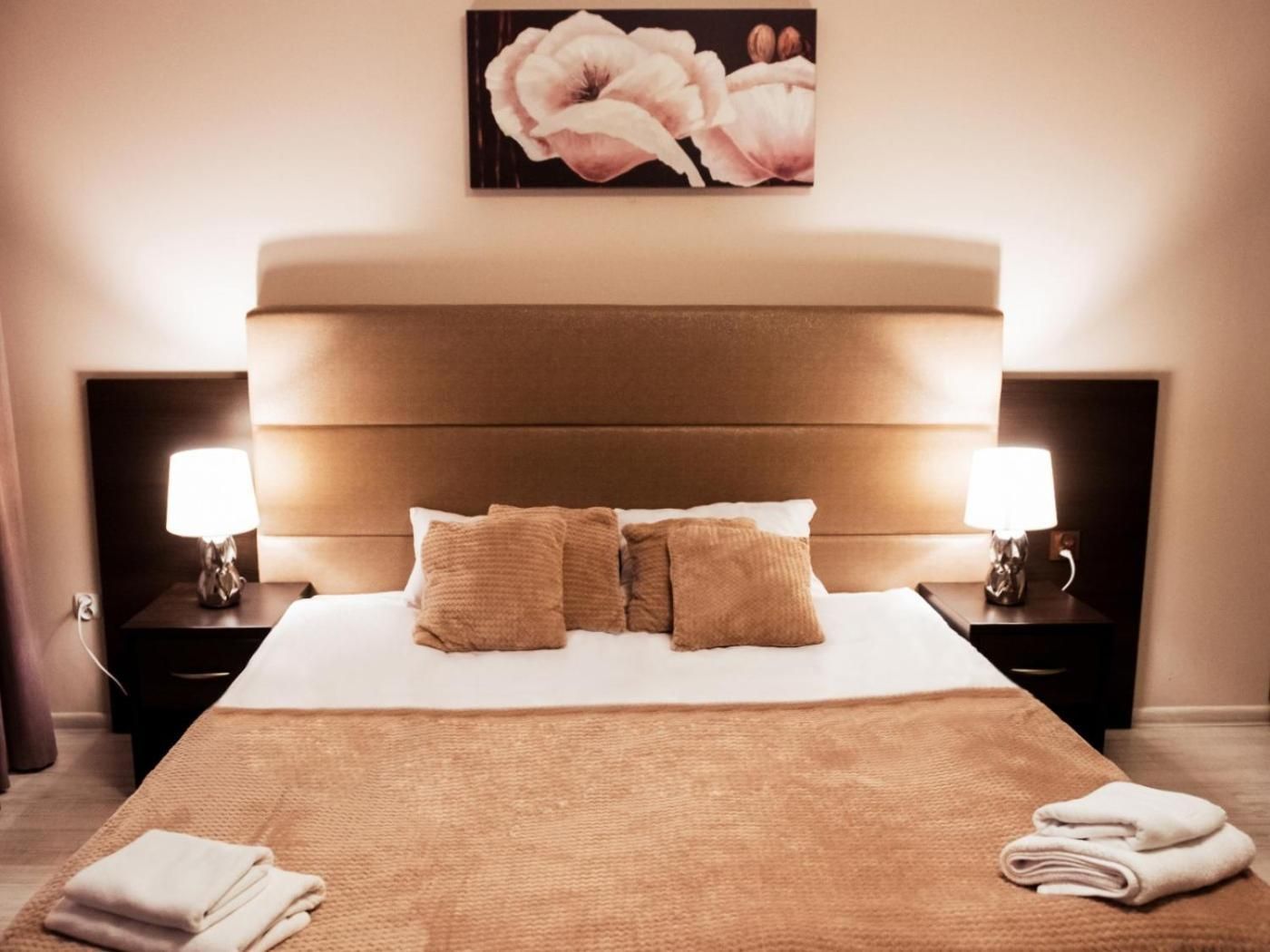 A hotel room with a large bed, two bedside tables, and a painting on the wall.
