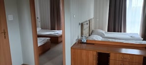 Une chambre d’hôtel avec deux lits simples, une commode en bois et une table de chevet avec une lampe.