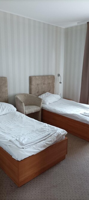 Habitación de hotel con dos camas individuales, una silla y una mesita de noche.