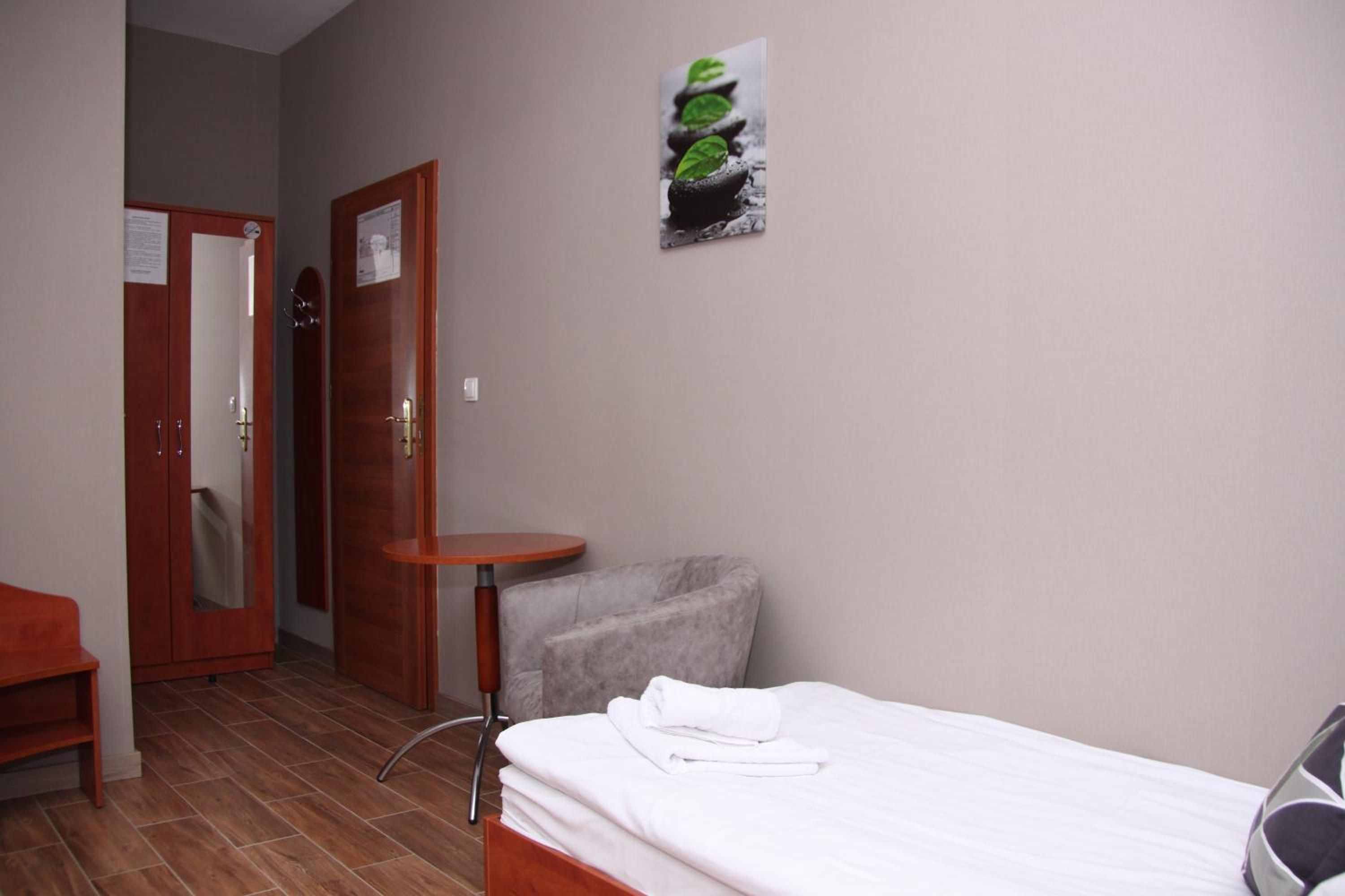 A hotel room with a bed, a small round table, a chair, a wardrobe, and a poster on the wall.