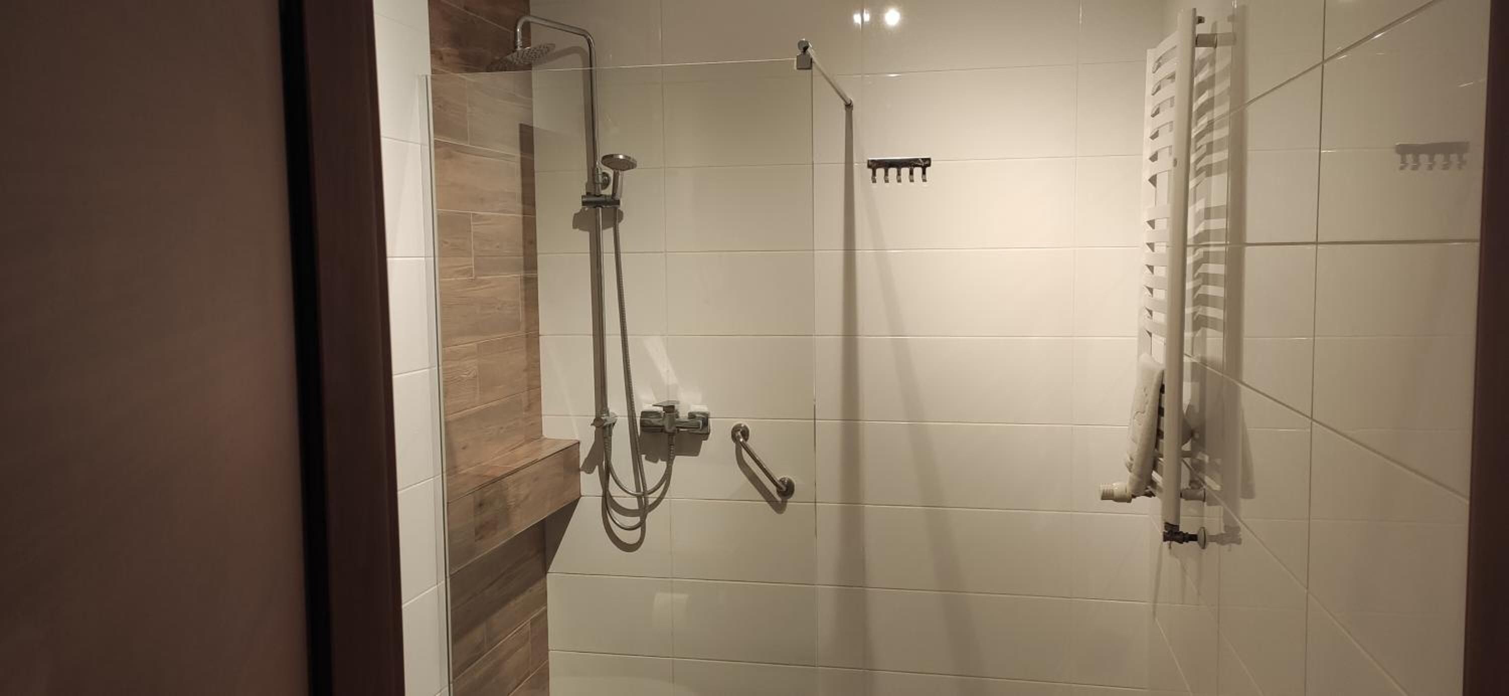 Ducha con cabezal de ducha de mano, panel de control en la pared y un perchero para toallas.