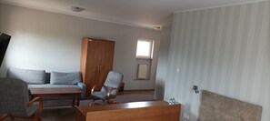 Una habitación con sofá, una mesa de madera, una silla, armario, radiador y ventana.