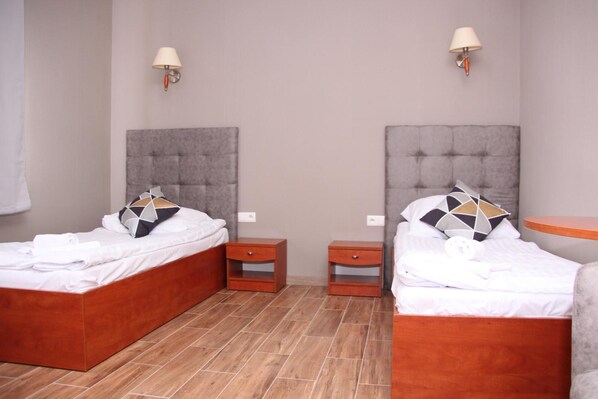 Una habitación de hotel con dos camas, cada una con cabecera, mesita de noche y lámpara.
