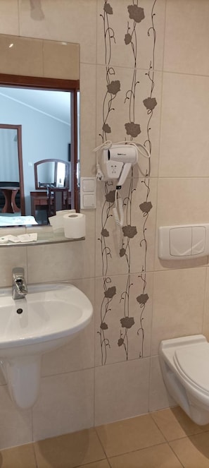 Uma casa de banho com uma pia branca, um espelho, um secador de cabelo e uma sanita.