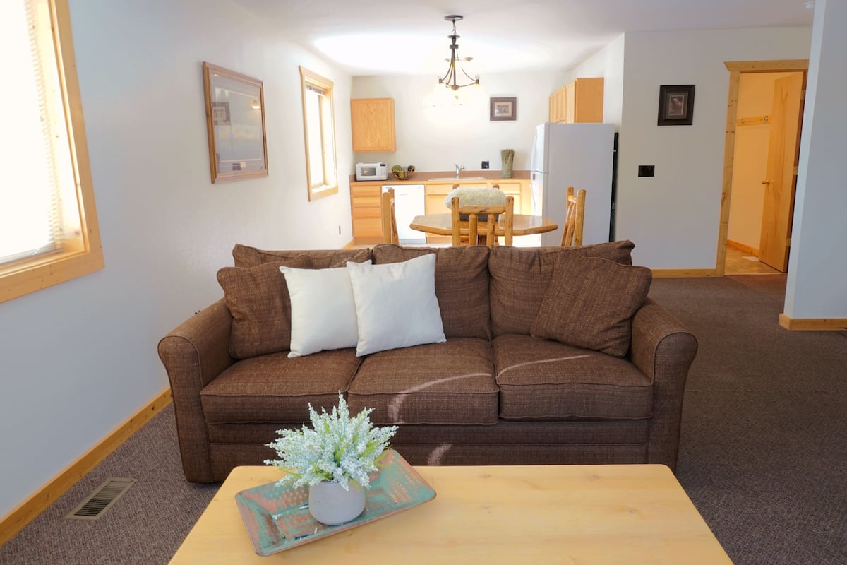 A living room with a brown sofa, a wooden coffee table, and a dining area with a wooden table and chairs.