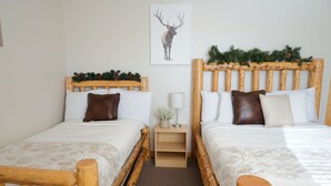 A double room with two wooden beds, a small bedside table with a lamp, and a framed deer picture on the wall. - The Aspen (West Yellowstone)