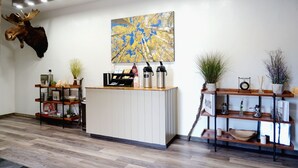 A reception area with a moose head mounted on the wall, a large abstract painting, and shelves with plants and decorative items. - The Aspen (West Yellowstone)