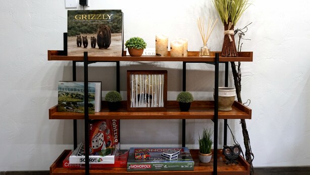 A wooden shelf with books, candles, and decorative items. - The Aspen (West Yellowstone)