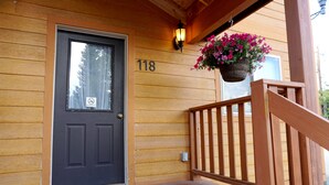 A wooden door with the number 118, a hanging flower basket, and a wooden railing. - The Aspen (West Yellowstone)
