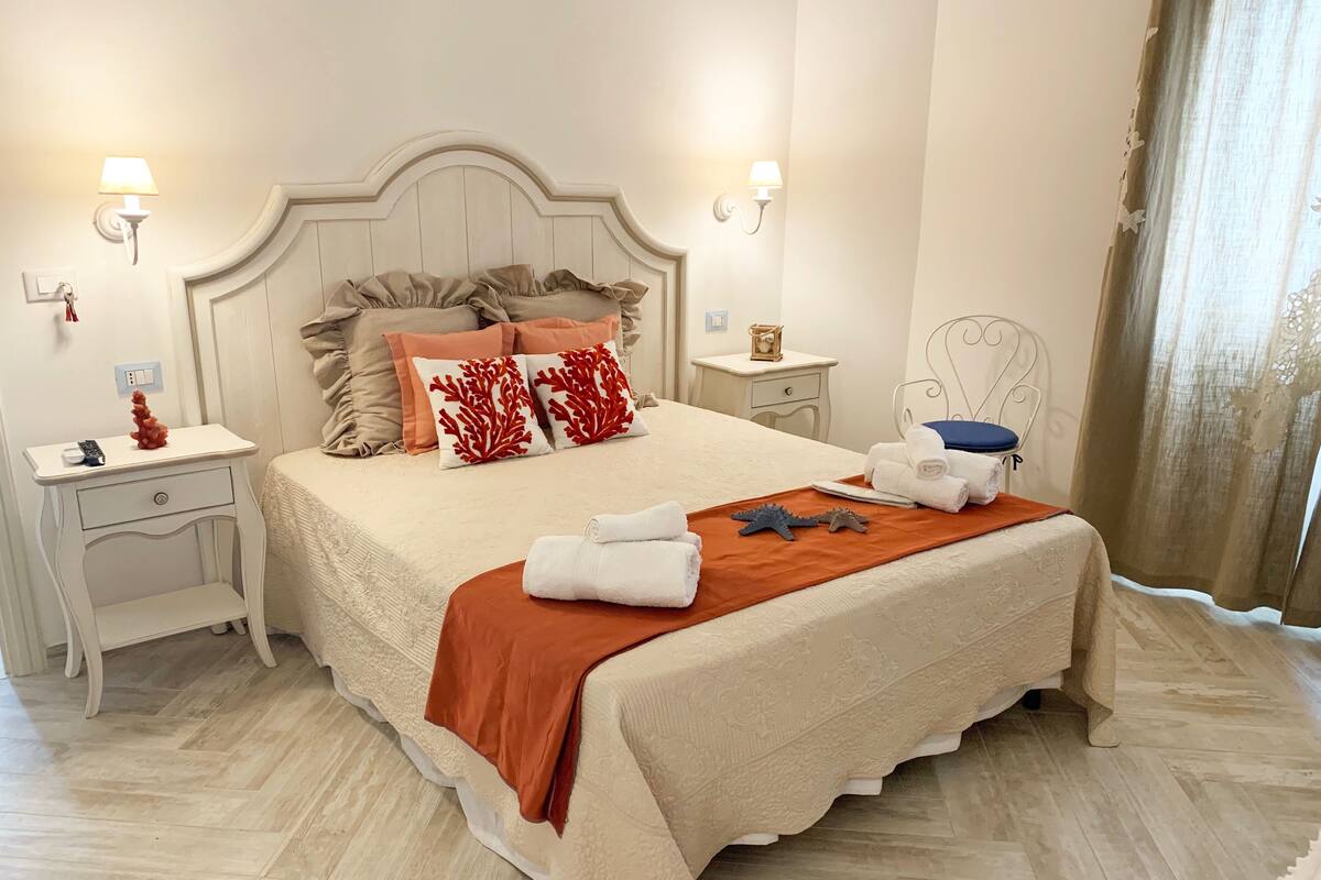 A neatly made bed with a white headboard, two bedside tables with lamps, and a nightstand with a lamp.