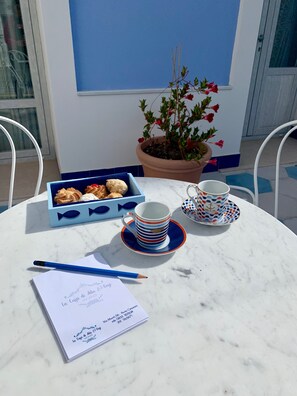 Ein Tisch mit einer blauen Kiste Gebäck, zwei gemusterten Tassen, einem blauen Bleistift und einem Papierstück mit Text.