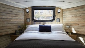 A bedroom with a wooden wall design, a large window, and a bed with white bedding and a blue pillow. - The Boathouse London (London)
