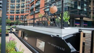 A modern boat with "The Boathouse" written on its side, docked in an urban setting with a building in the background.