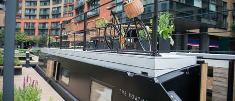 A modern boat with "The Boathouse" written on its side, docked in an urban setting with a building in the background.