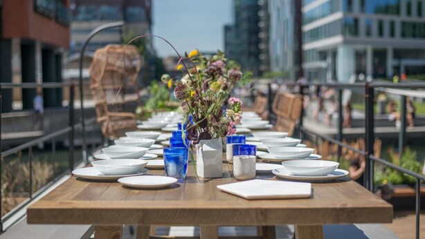 A long dining table set with plates, bowls, and blue glasses, centered with a floral arrangement. - The Boathouse London (London)
