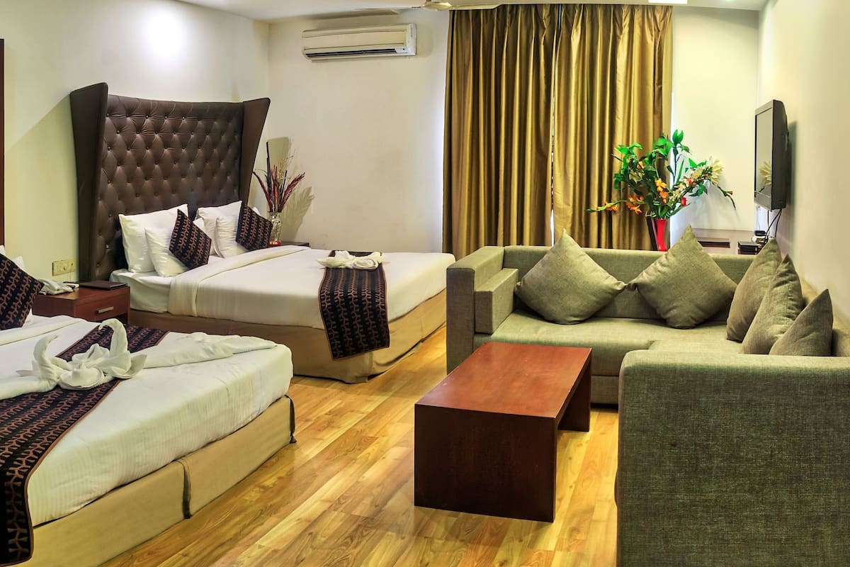 A hotel room with a large bed, a sofa, a coffee table, and a TV.