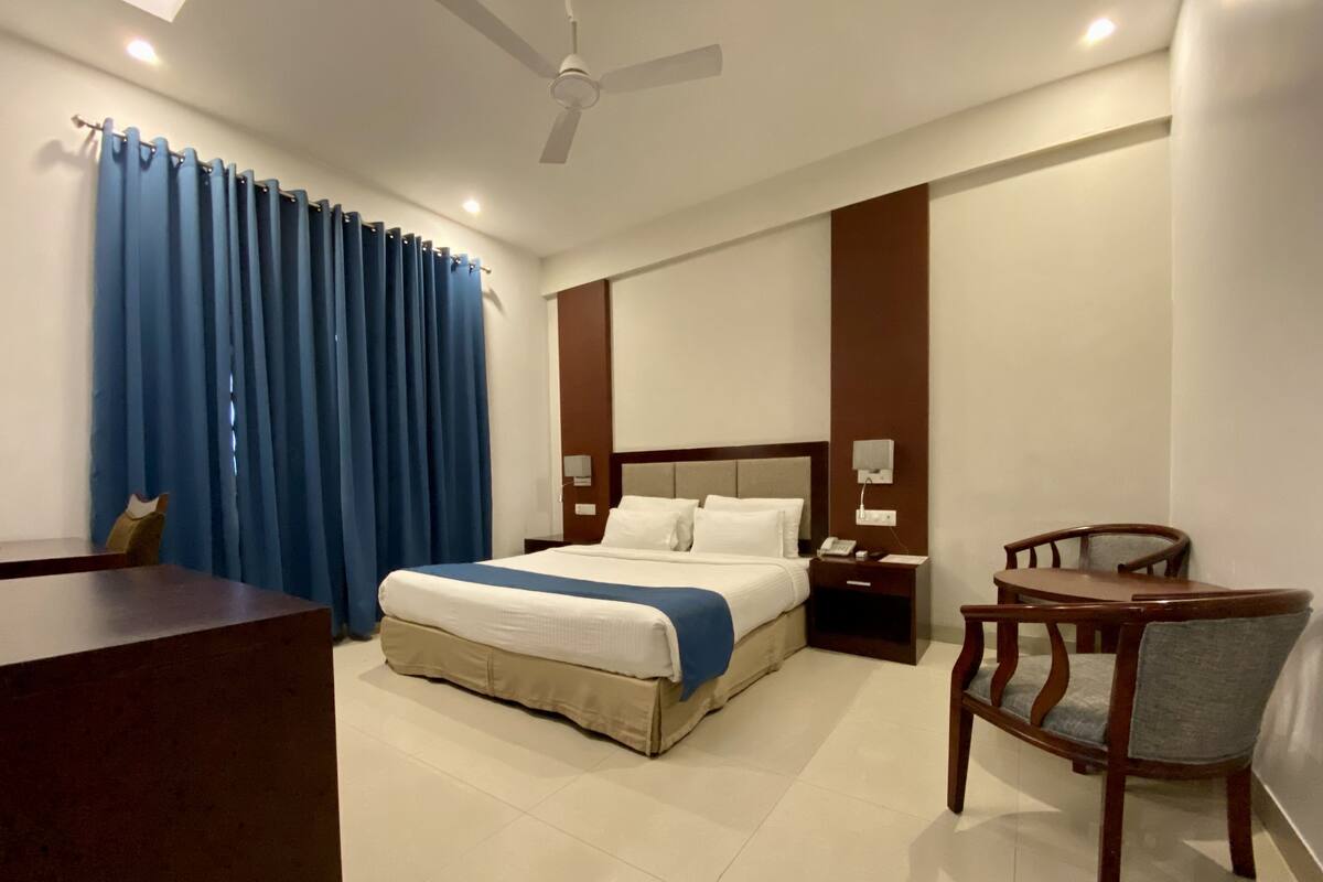 A hotel room with a bed, bedside table, chair, and a desk.