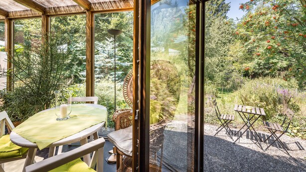 Ein Wintergarten mit Tisch und Stühlen, umgeben von üppigem Grün und verschiedenen Pflanzen.