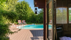 Eine Holzterrasse mit Pool, Liegestühlen und Blick ins grüne Umland.
