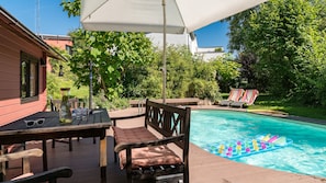 A poolside area with a wooden deck, lounge chairs, and a table with glasses and sunglasses. - Entspannen im Taunus (Taunusstein)