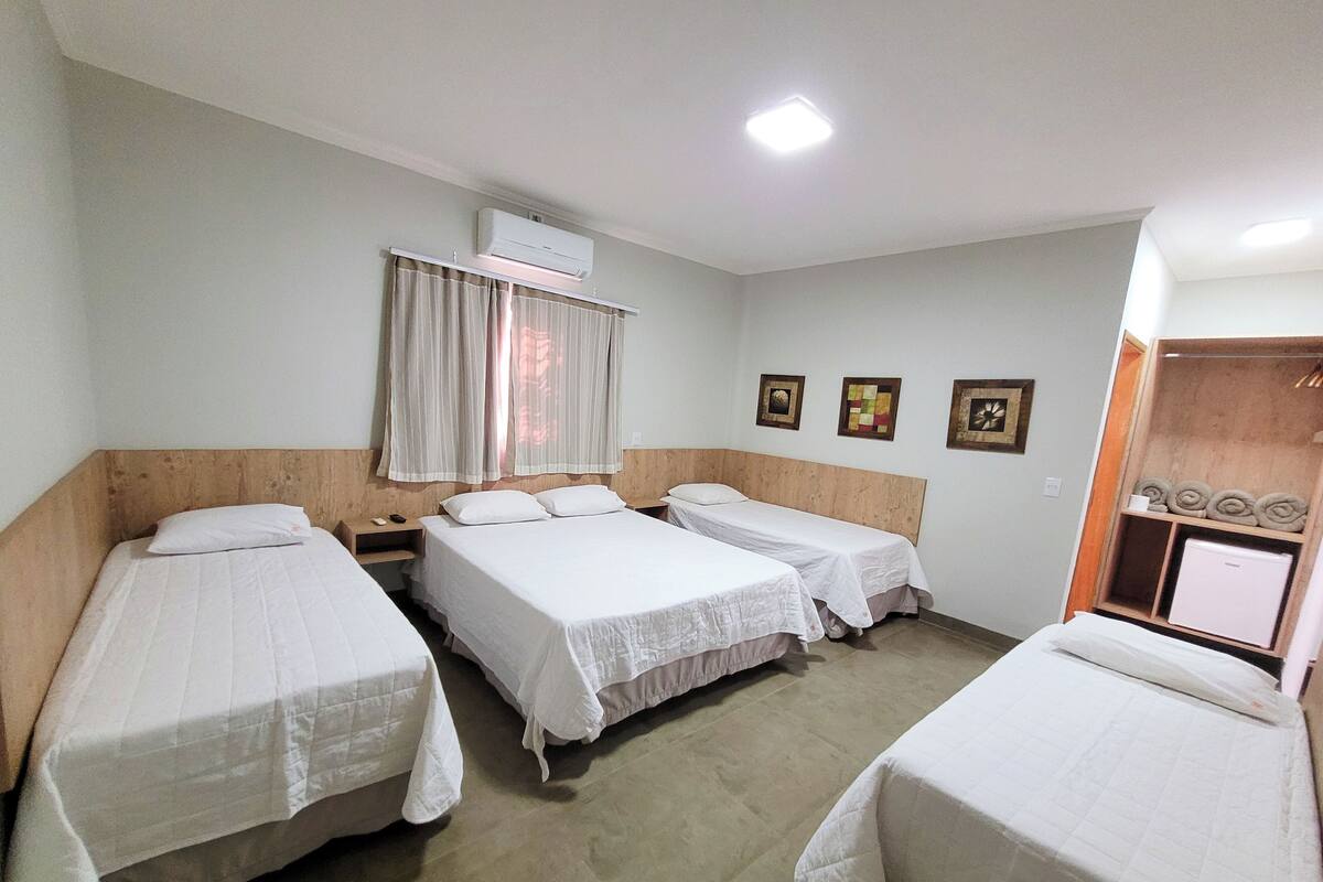 A hotel room with four single beds, a wardrobe, a small desk, and a wall-mounted air conditioner.