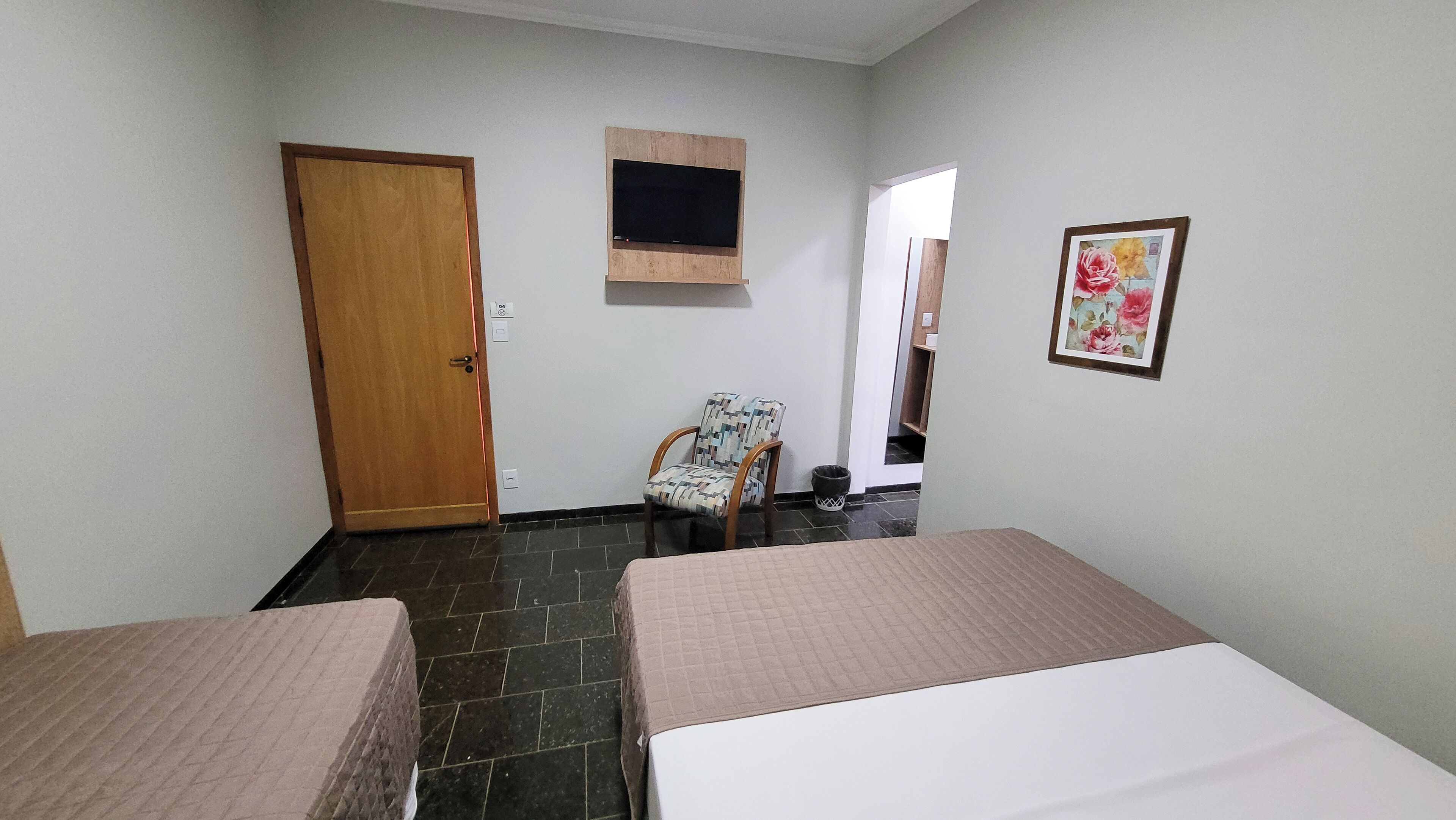 A room with two beds, a chair, a TV mounted on the wall, and a door.