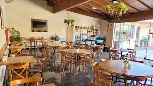 Un café espacioso con mesas y sillas de madera, una zona de bar y plantas colgantes.
