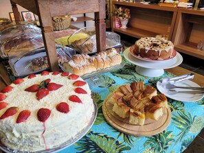 Una mesa de buffet con diversos postres, incluyendo pasteles y repostería, cubierta con plástico transparente.