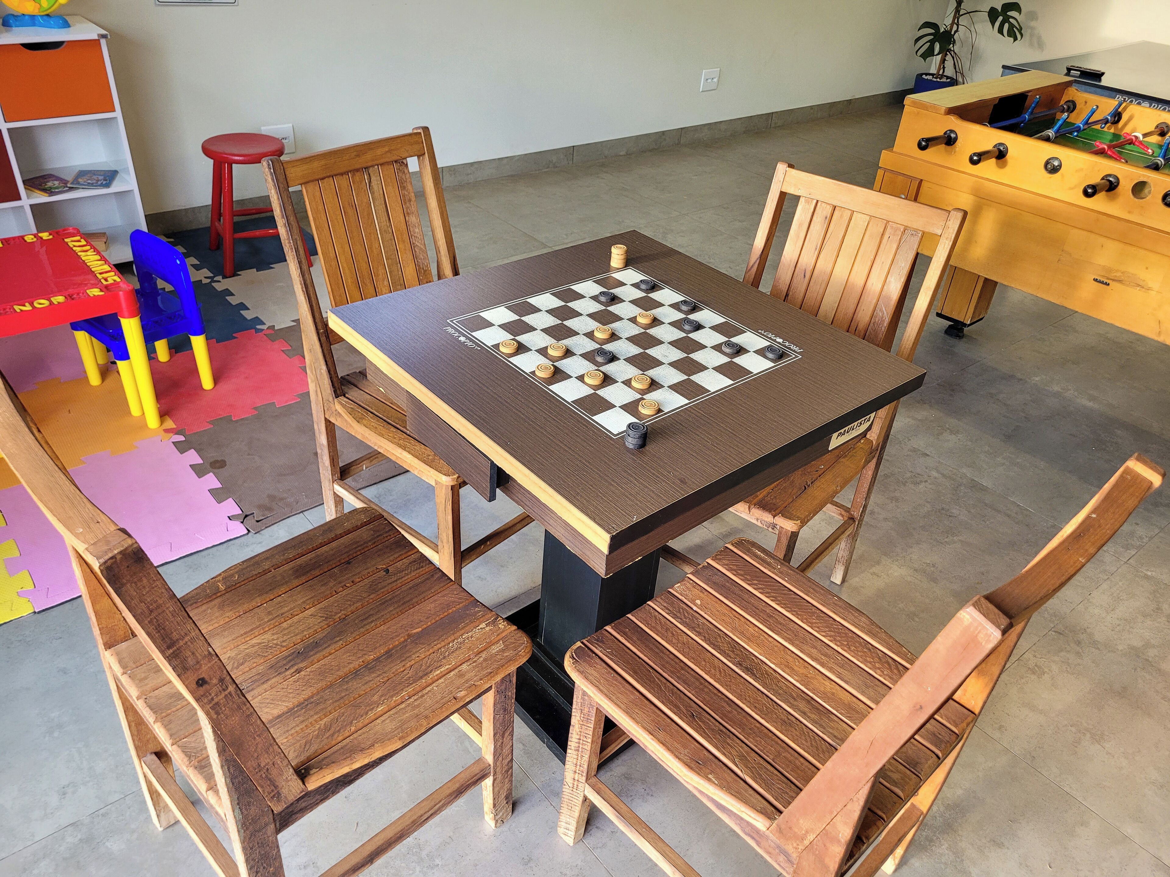 Una mesa de madera con un tablero de juego de cuadros, rodeada de sillas de madera.