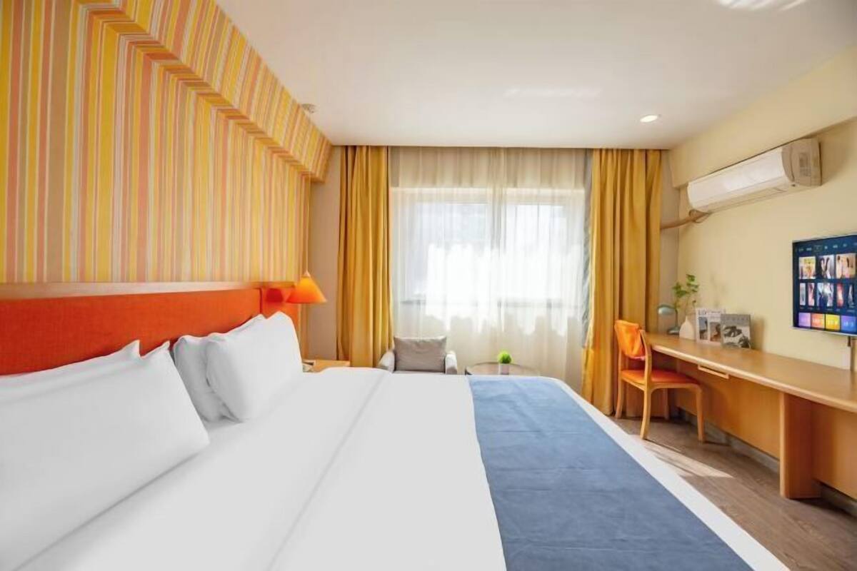 A hotel room with a bed, desk, chair, and window with curtains.