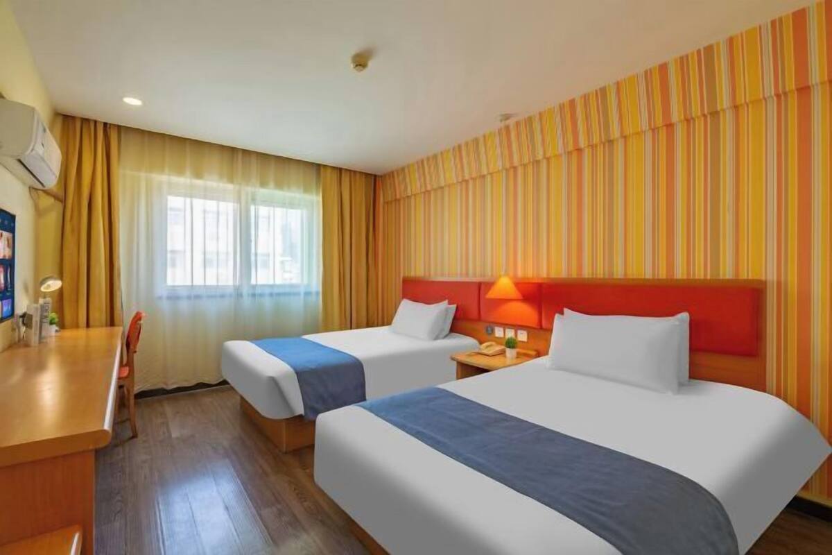 A hotel room with two beds, a desk, a chair, and a window with curtains.
