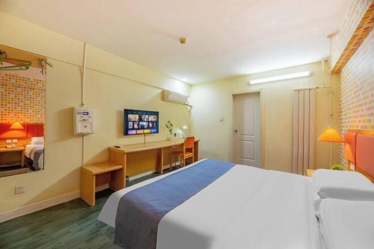 A hotel room with a bed, a desk, a chair, a TV, and a bathroom.